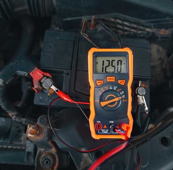 Un multimetro digitale posizionato su un batteria di auto, con il display che mostra la lettura di 12.50 volt, utilizzato per misurare la tensione della batteria.