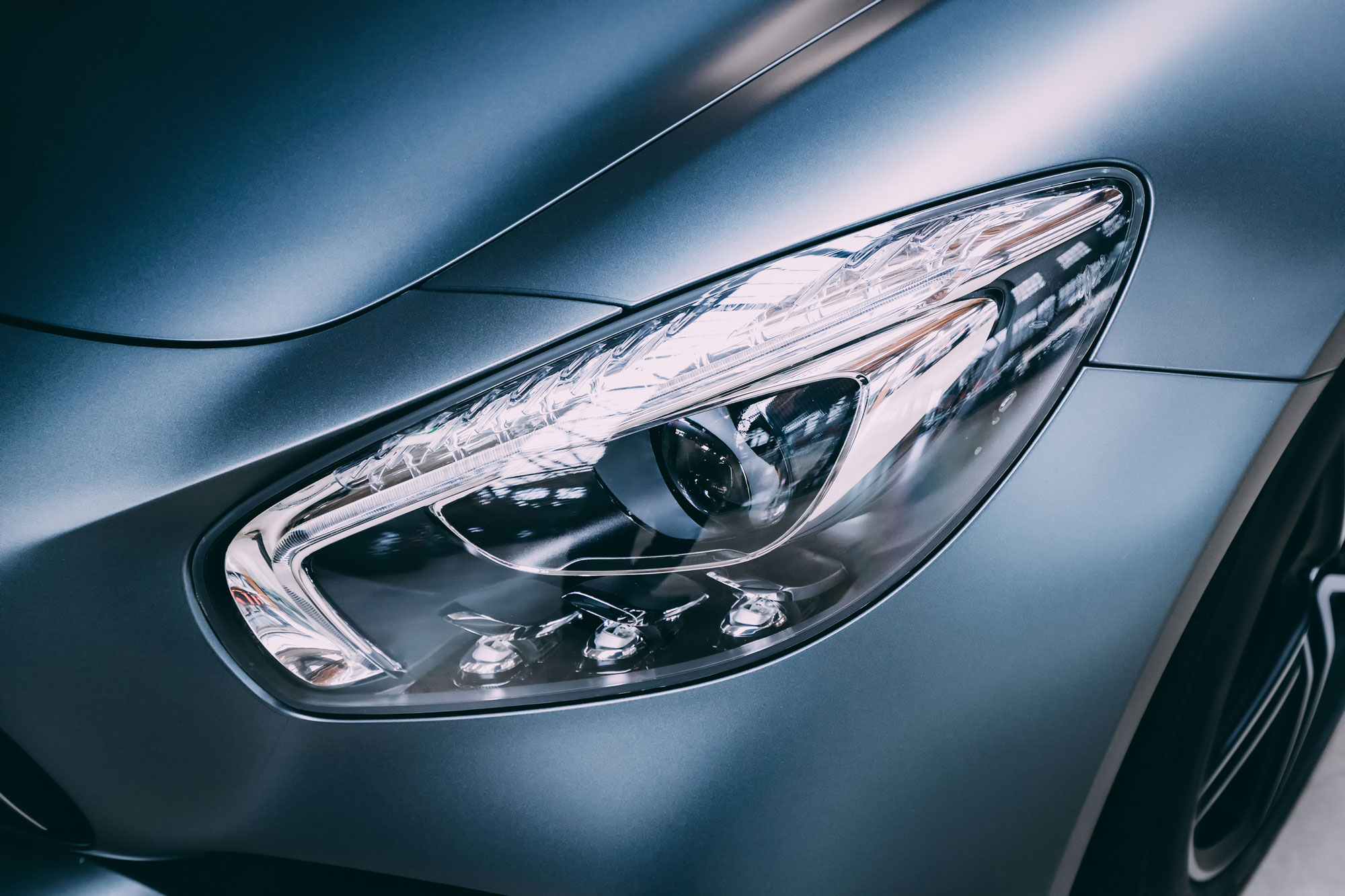 Dettaglio di un faro di un'auto moderna con finitura opaca, evidenziando il design elegante e le luci LED.