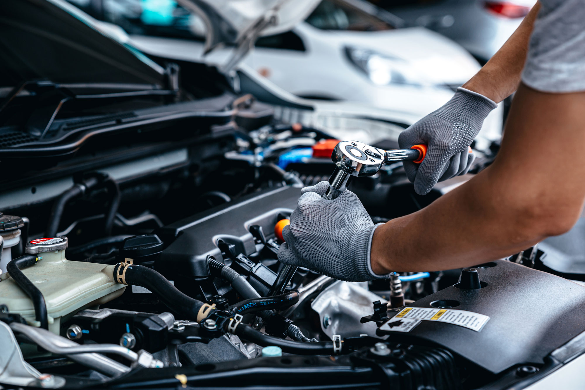 Un meccanico indossa guanti mentre utilizza una chiave dinamometrica per lavorare su un motore di automobile.