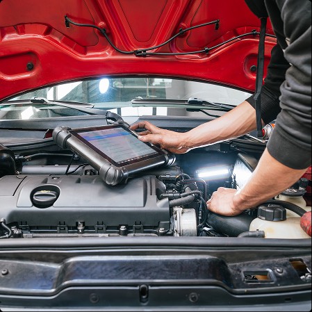 Un meccanico utilizza un dispositivo diagnostico elettronico per controllare il motore di un'auto rossa. L'immagine mostra dettagli del motore e dell'attrezzatura.